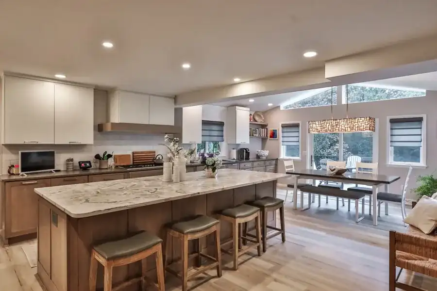 Kitchen remodeling in Albany, NY: open kitchen with white upper cabinets, wood base cabinets and a long granite island with seating