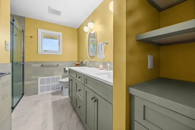 Bathroom with sage green vanity, white quartz top, sliding glass shower door and gold painted walls