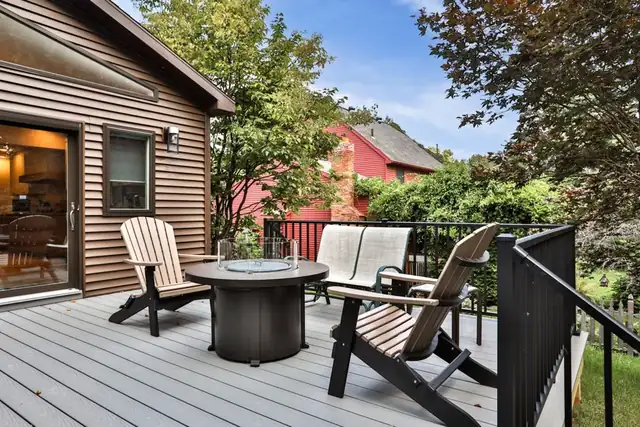 Gray composite deck with black railings and Adirondack chairs off the back of a brown-sided home