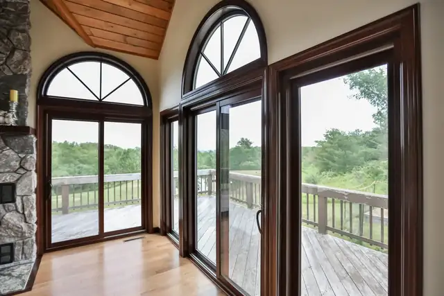 Bright room with arched dark wood windows, sliding patio doors and a stone wall opening onto a deck