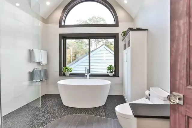 Saratoga Springs, NY bathroom remodel with freestanding tub under an arched window, pebble tile floor and walk-in shower