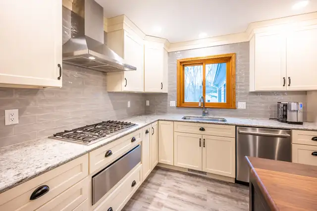 Kitchen with cream cabinets, a stainless range hood, gray tile backsplash and granite counters around a gas cooktop
