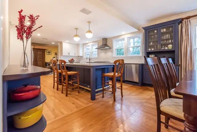 Loudonville kitchen and dining room with a navy island, white cabinets, brass pendants, a navy glass-front hutch and oak floors